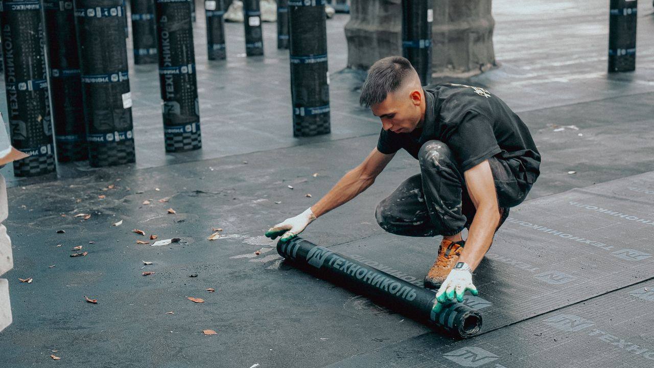 Worker rolling out a waterproofing membrane on a roof